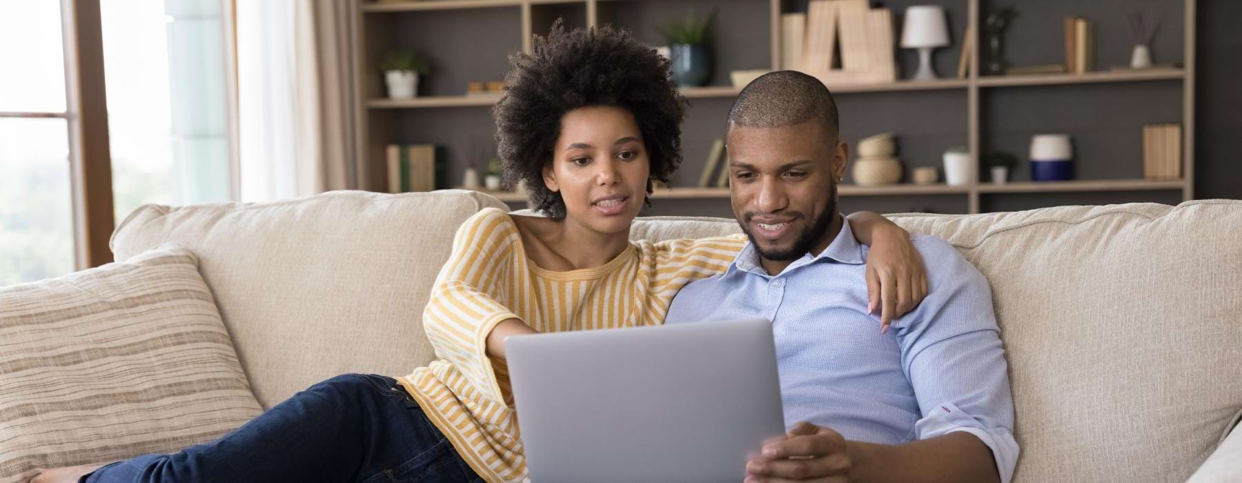 a man and a woman sitting on a couch looking at a laptop